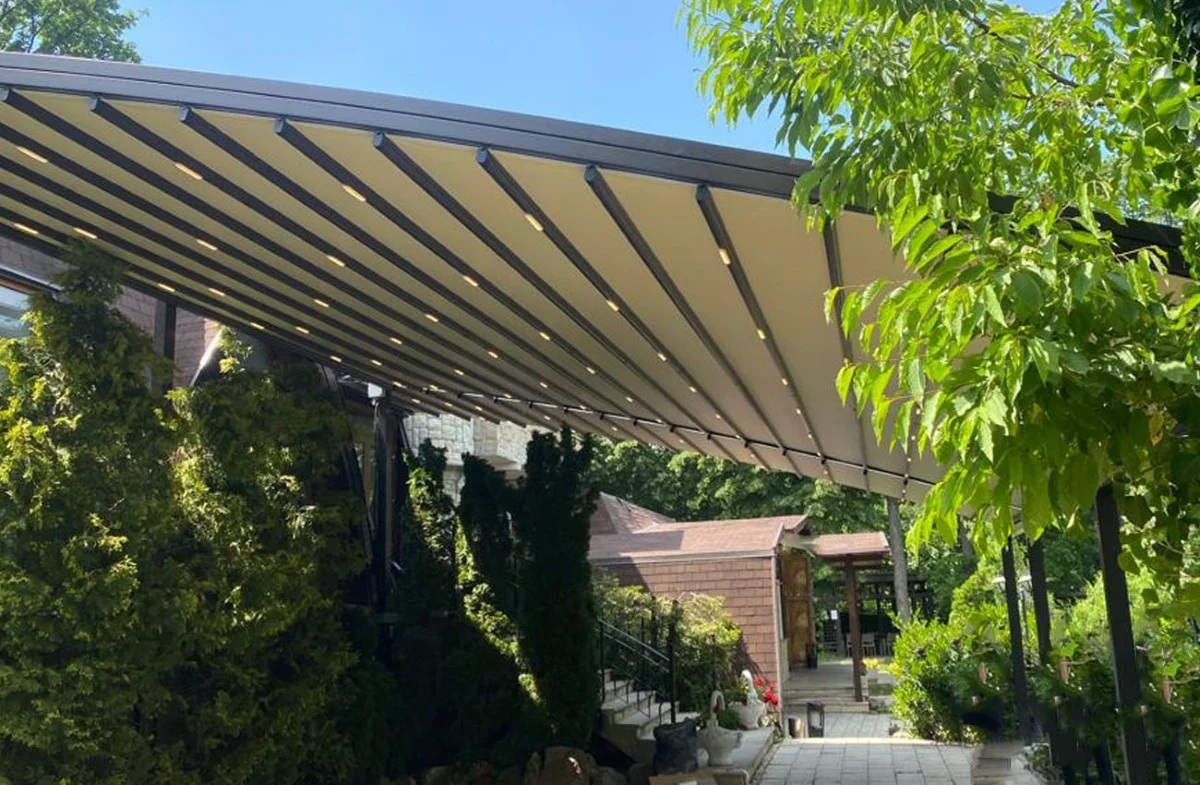Pérgola retráctil Arcodia Pérgola retráctil Arcodia con membrana curvada en un jardín